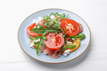 Tasty salad with arugula, cheese, tomatoes, nuts and prosciutto on white wooden table, closeup