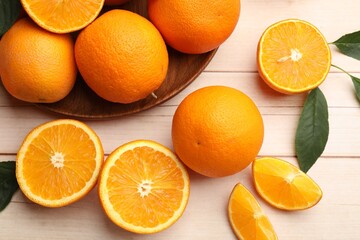 Fresh ripe oranges and leaves on light wooden table, flat lay