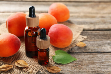 Aromatic essential oil in bottles, seeds, leaf and ripe apricots on wooden table, closeup