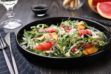 Tasty salad with arugula, cheese, grapefruit, vegetable and balsamic sauce on dark wooden table, closeup