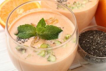 Superfood. Tasty smoothie with chia seeds, mint, pistachio and orange in glasses on white wooden table, closeup