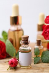 Bottles of essential oils, red roses and herbs on wooden table, closeup