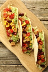 Tasty vegetarian tacos with beans, tofu and vegetables on wooden table, top view