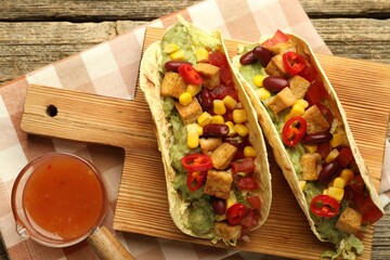 Tasty vegetarian tacos served with sauce on wooden table, flat lay