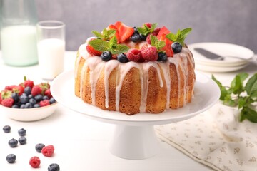 Delicious bundt cake with berries, glaze and mint on white table against grey background, closeup