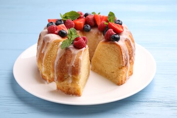 Pieces of delicious bundt cake with berries, glaze and mint on light blue wooden table, closeup