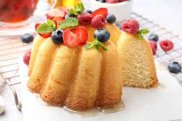 Tasty Bundt cake with berries, honey and mint on table, closeup