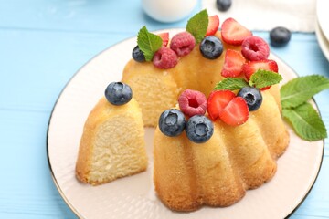 Tasty Bundt cake with berries and mint on light blue wooden table, closeup