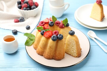 Tasty Bundt cake with berries, honey and mint on light blue wooden table, closeup