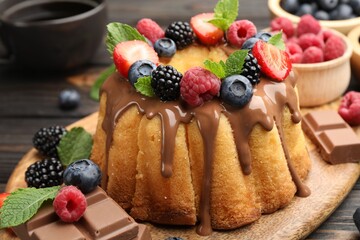 Tasty Bundt cake with berries, chocolate, mint and coffee on wooden table, closeup