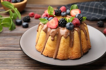 Tasty Bundt cake with berries, chocolate and mint on wooden table, closeup