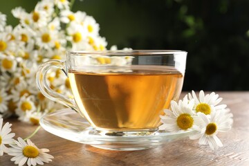Aromatic tea in glass cup and chamomile flowers on wooden table, closeup
