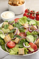 Delicious salad with croutons and vegetables served on light grey table, closeup