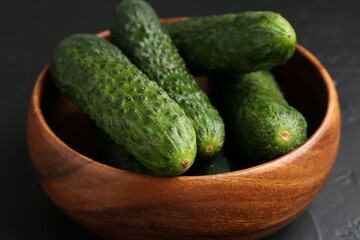 Fresh cucumbers in bowl on dark textured table, closeup