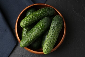 Fresh cucumbers in bowl on dark textured table, top view