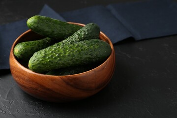Fresh cucumbers in bowl on dark textured table, closeup