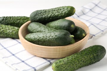 Fresh cucumbers, napkin and bowl on white wooden table, closeup