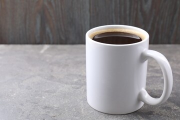 Aromatic coffee in cup on grey textured table against dark wooden background, closeup. Space for text