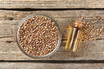 Coriander essential oil in bottle and seeds on wooden table, flat lay