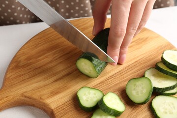 Woman cutting fresh cucumber at white table, closeup