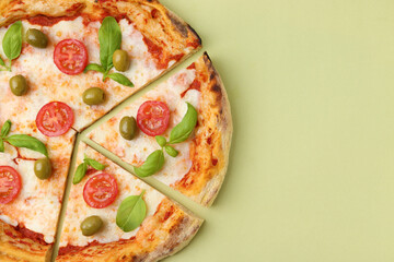 Delicious cut pizza with tomatoes, basil and olives on light green background, top view. Space for text