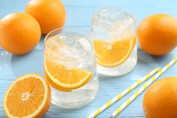 Sparkling water with orange slices in glasses, fresh fruits and straws on light blue wooden table,...