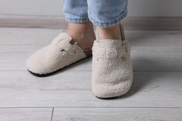 Woman in soft white slippers on light wooden floor, closeup