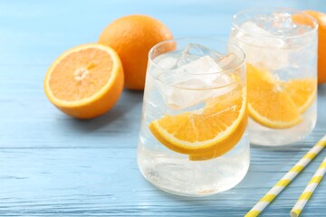 Sparkling water with orange slices in glasses, fresh fruits and straws on light blue wooden table,...