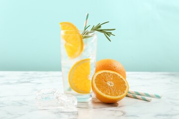 Refreshing soda drink with orange slices and rosemary in glass on white marble table