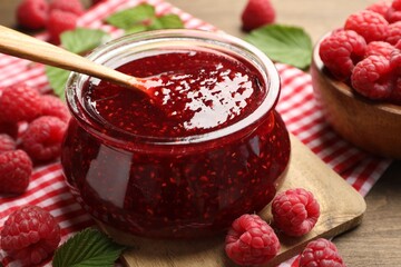 Tasty jam, fresh ripe raspberries and leaves on wooden table, closeup.