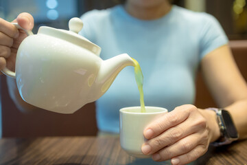 Close-up of a woman pouring green tea from a kettle into glasses