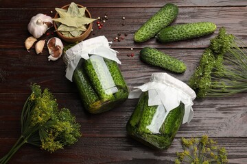 Fototapeta premium Pickled cucumbers in jars, fresh ones, garlic, dill and dry bay leaves on wooden table, flat lay