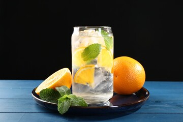 Sparkling water with orange, ice and mint in glass on blue wooden table, closeup