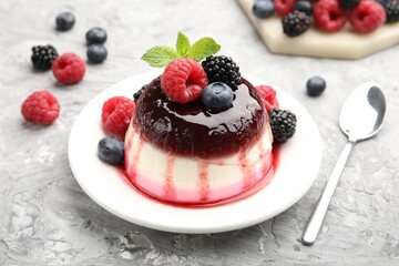 Tasty panna cotta with berries and jam on light grey table, closeup
