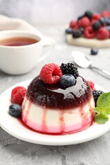 Tasty panna cotta with berries and jam on light grey table, closeup