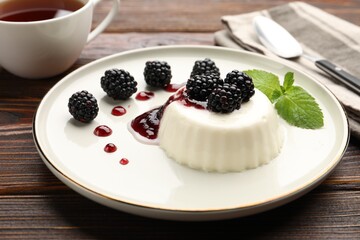 Tasty panna cotta with blackberries, mint and sauce on wooden table, closeup