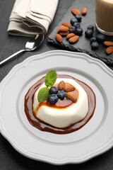 Tasty panna cotta with blueberries, almonds and sauce on black table, closeup