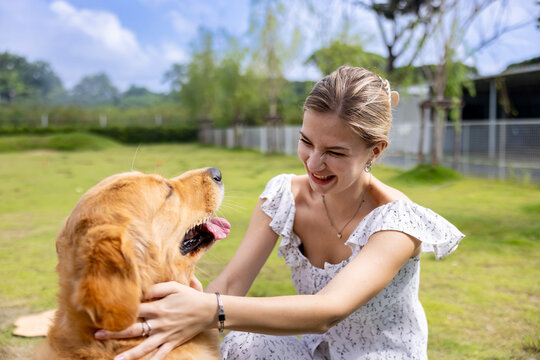 Caucasian woman hugging her cute energetic golden retriever dog in the outdoor park during summer for animal lover and pet sitter training concept