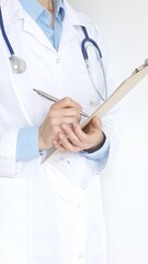 Unknown female doctor wearing stethoscope and white coat over blue blouse is standing and writing...