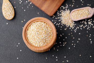 Quinoa seeds in multiple wooden bowls and spoons on dark background