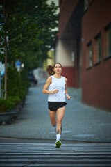 Young woman running along city street during early morning light for exercise. Concept of confidence, positive energy, urban jogging ritual, and women healthy lifestyle.