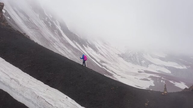 Lonely female backpacker dressed rain cover with backpack and trekking poles making acclimatization trek around Lenin peak base camp climbing Petrovsky Peak 4910 m, Pamir mountains range, Kyrgyzstan.