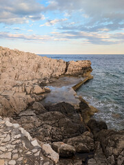 A picturesque rocky shore with a man-made swimming platform and a natural pool under a beautiful, cloudy evening sky.