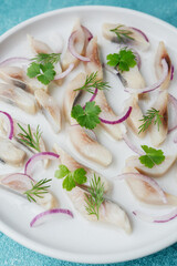Marinated herring slices with red onion and herbs on white plate over blue background
