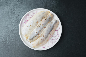 Marinated herring fillets with coriander seeds and onion on white plate over dark background