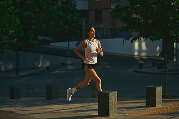 Female jogger in the early morning running along an urban street wearing casual sportswear. Concept...