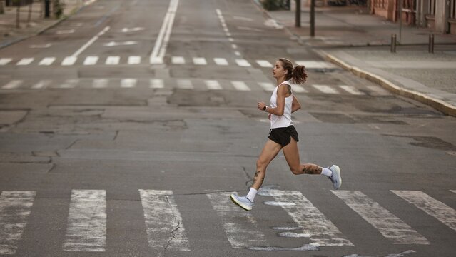 Female jogger running along city road for morning exercise. Concept of motion momentum, feminine power, running form, and confidence in movement. - Powered by Adobe
