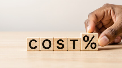 Wooden COST blocks with a hand placing a down arrow and percent sign, bright scene, clear business theme for savings or decrease.