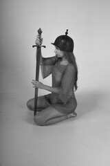 Female warrior in chainmail and original ancient helmet sitting on her knees and holding sword...