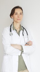 Female medical professional in white lab coat, stethoscope draped, standing with crossed arms and...